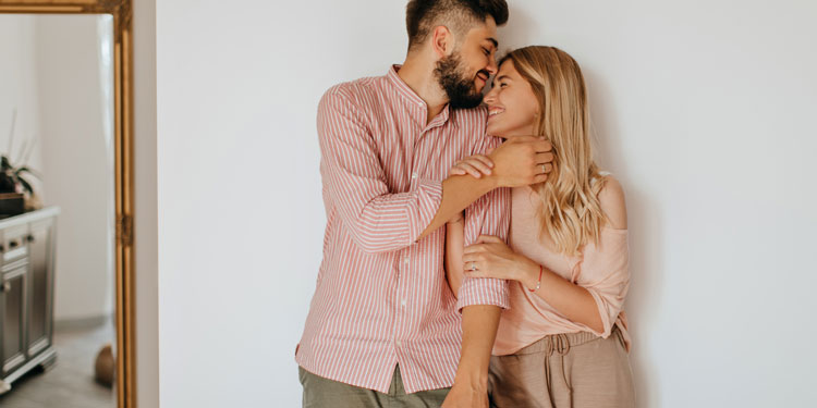 man and woman standing at the wall and hugging; the man kisses her forehead