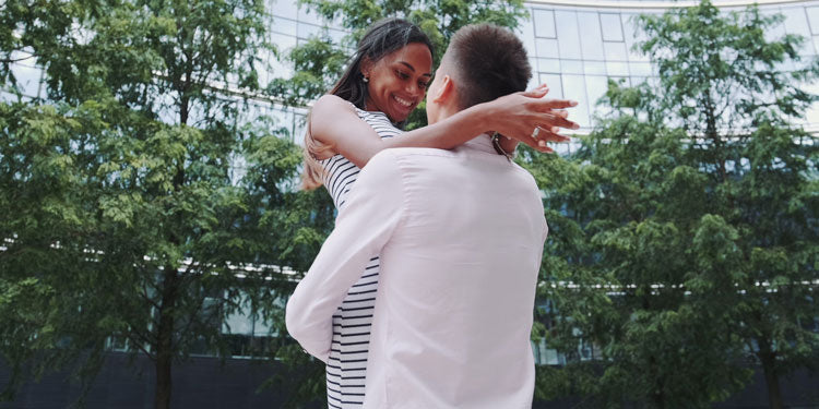 young couple standing in a park and hugging, the woman smiles at the man