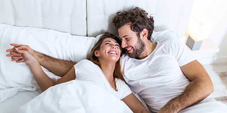 a young couple laying in bed and smiling at each other