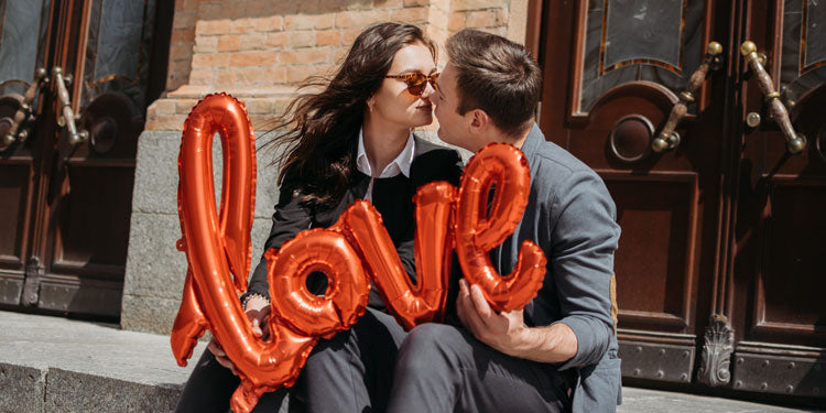 man and woman sitting in front of a building, holding a sign with "love" written on it