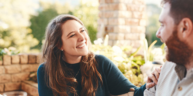 happy, joyful couple sitting outside, talking and smiling at each other, green plants and a terrace in the background