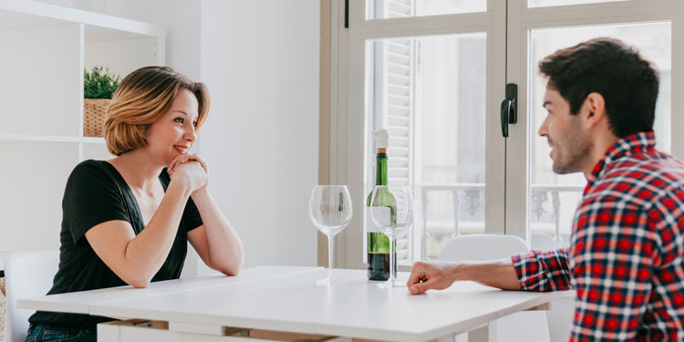 a couple sitting a a white table and talking and drinking wine, both are happy