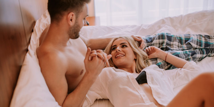 couple laying in bed and smiling at each other, both are happy