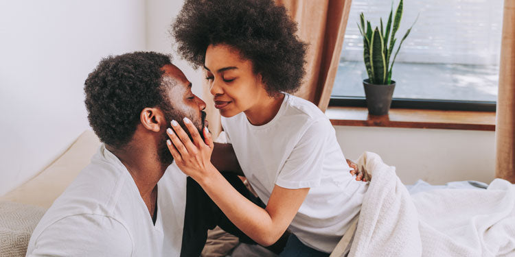 Afro-American couple sitting on bed and kissing, and smiling