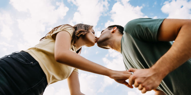 man and woman kissing; clouds in the background