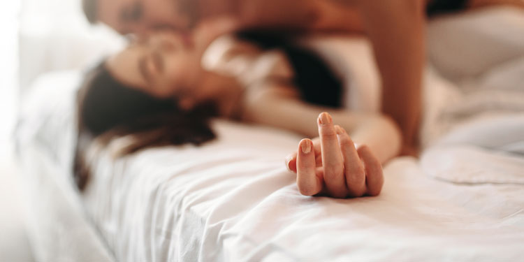 man and woman being sensual and playful on the bed; the hand is in the focus, man and woman is out of focuss