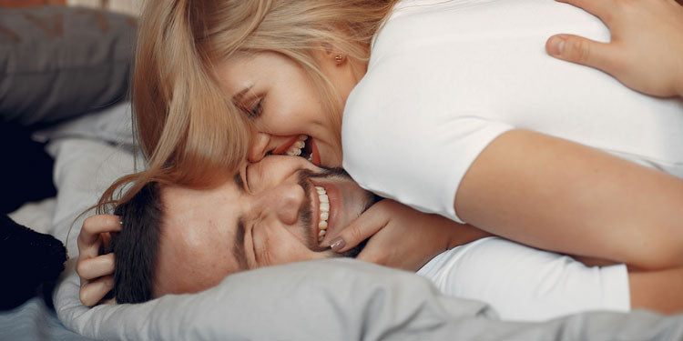 young couple being playful in bed; both are smiling and happy