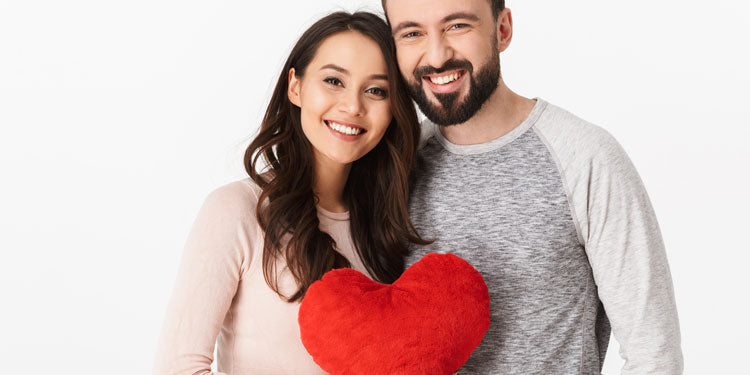 young happy couple posing for a portrait, both smiling and holding a red heart in front of them