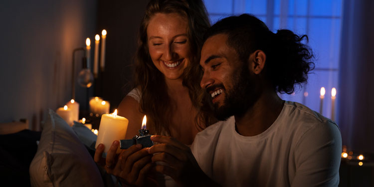 a young couple lighting up candles in a dimmed room, both are smiling