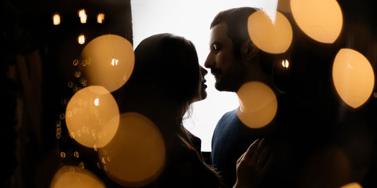 man and woman looking at each other almost kissing, blurred lights in the foreground