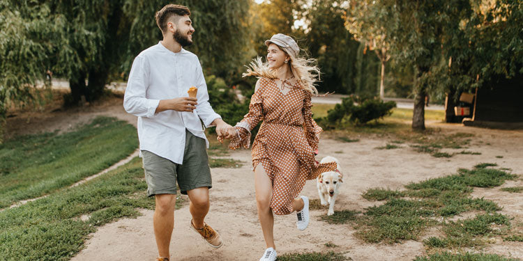 man, woman, and a dog are having a stroll in a park, man and woman are holding hands and smiling,