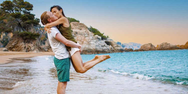 a man holds a woman off the ground at the beach
