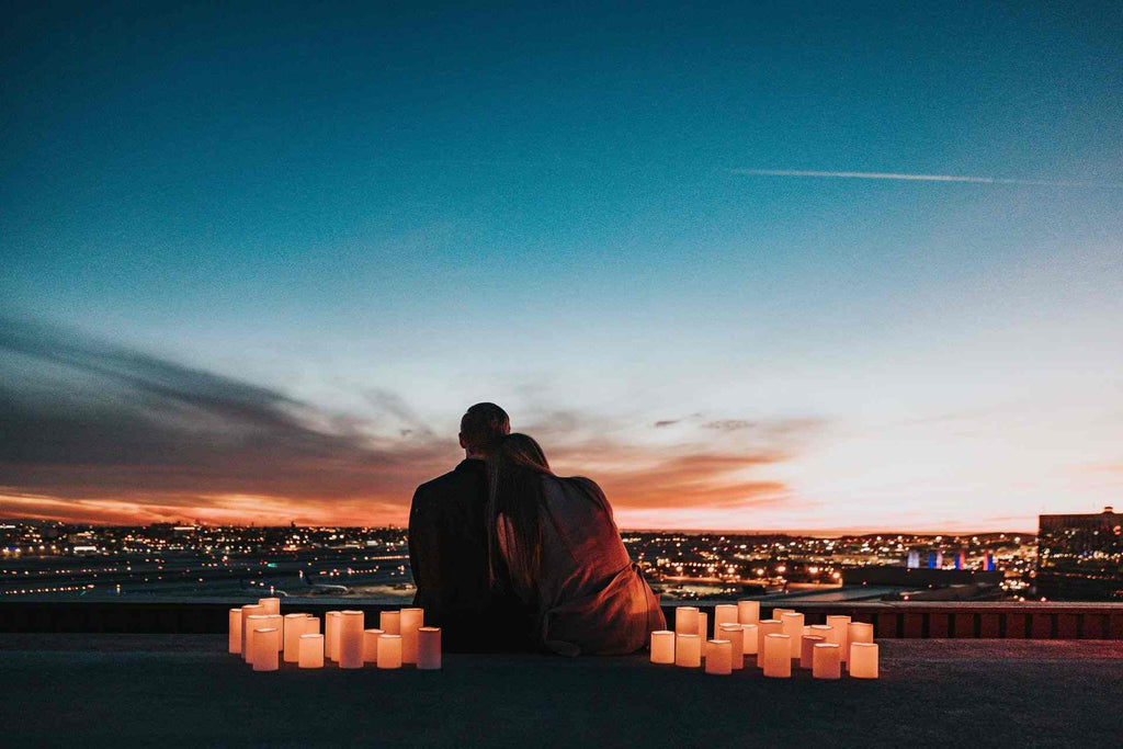 a couple sits surrounded by candles looking down on a city