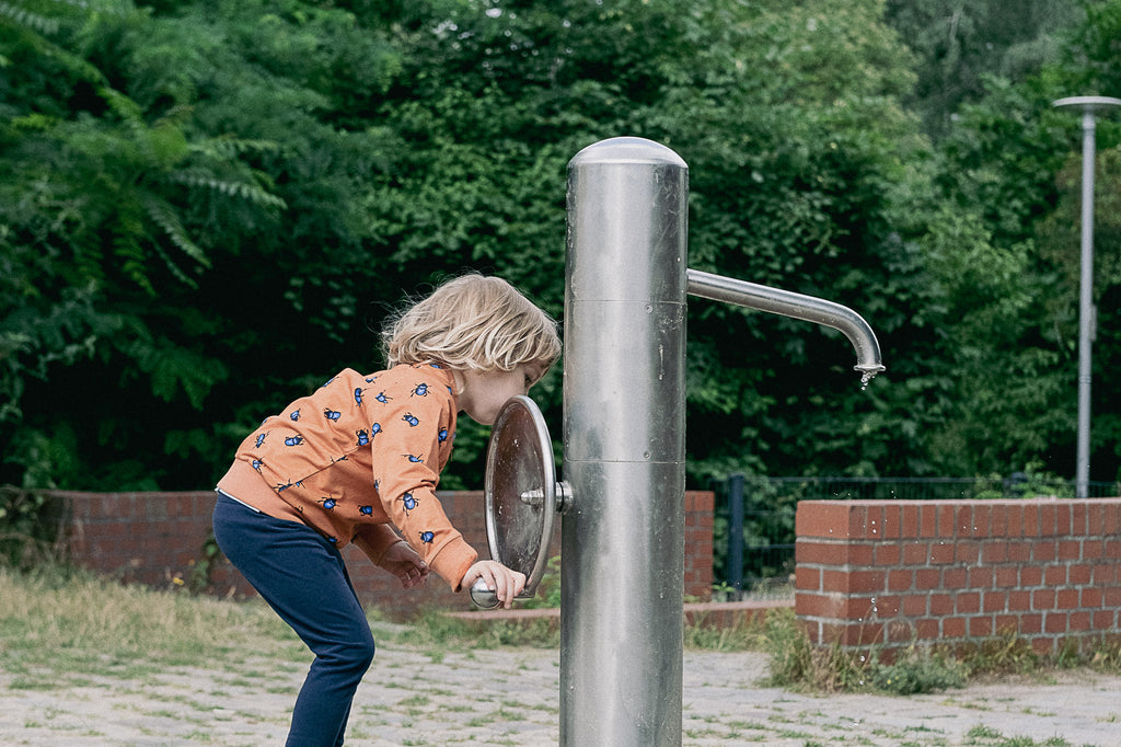 Child playing with water in a playground wearing the beetle bomber jacket