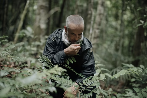 Man in black rain coat, in forest smelling plants