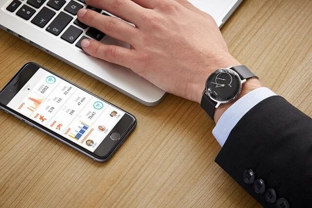 Smart phone next to hand with watch typing on computer