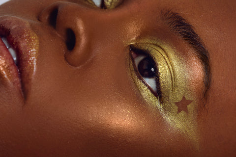 A close up image of a face of a woman that is wearing gold eyeshadow on her lids with a star just below her eyebrow bone