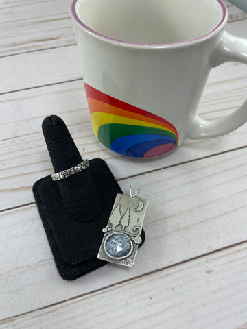 Beth Millner Jewelry pebble beach ring and starry winter sky dendritic opal wonderland pendant next to a coffee mug