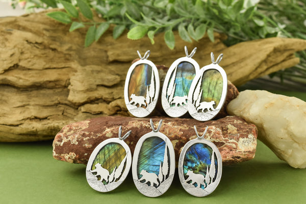Sterling silver pendants with a labradorite front and back. A bear walks along the bottom with two conifers behind it.