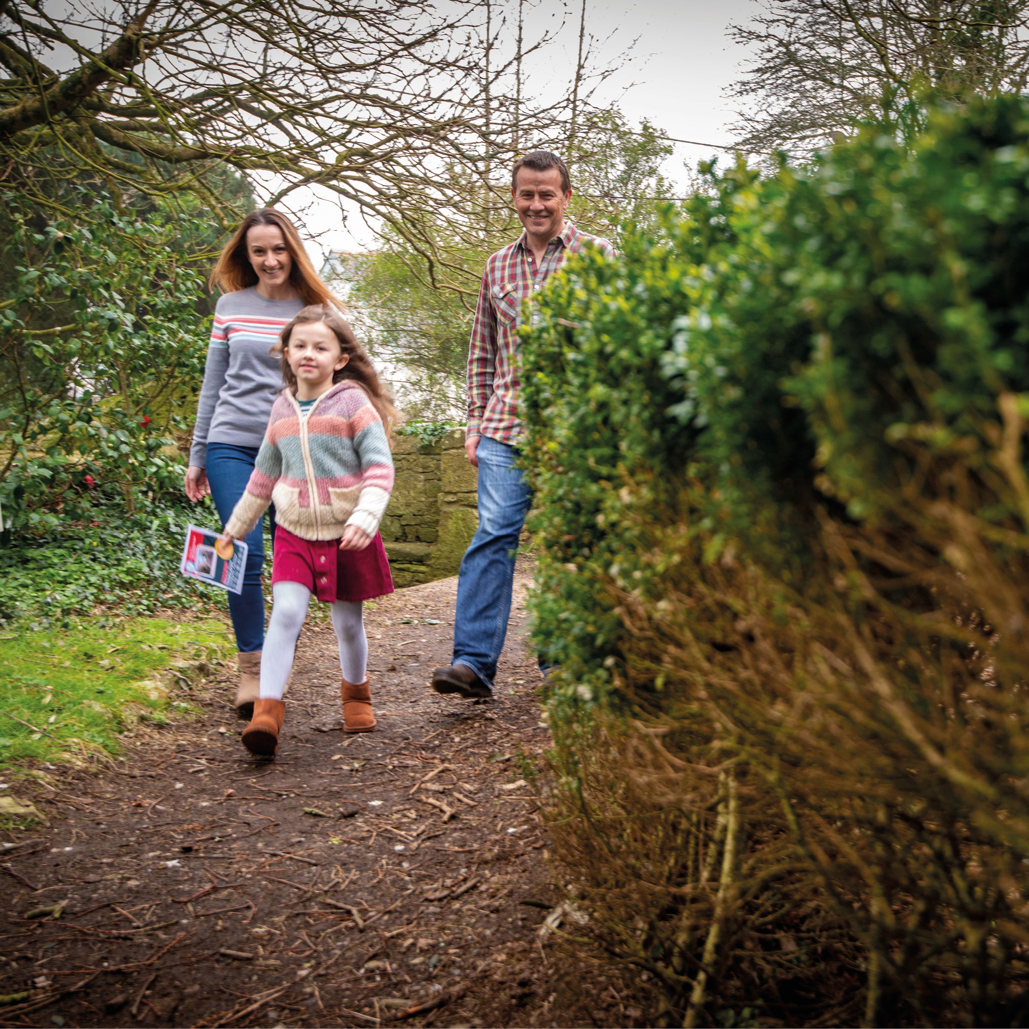 A family - mother, father and young daughter - walk along a path in the countryside on a Treasure Trail 