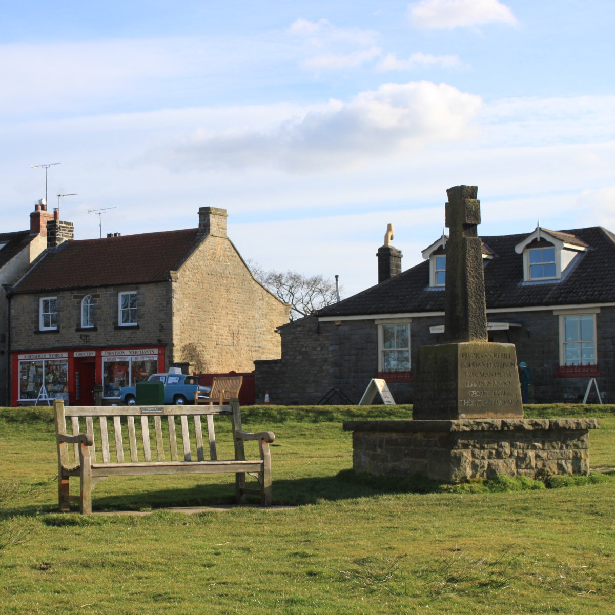 Goathland memorial cross with Aidensfield Stores and a 1960s police car in the background