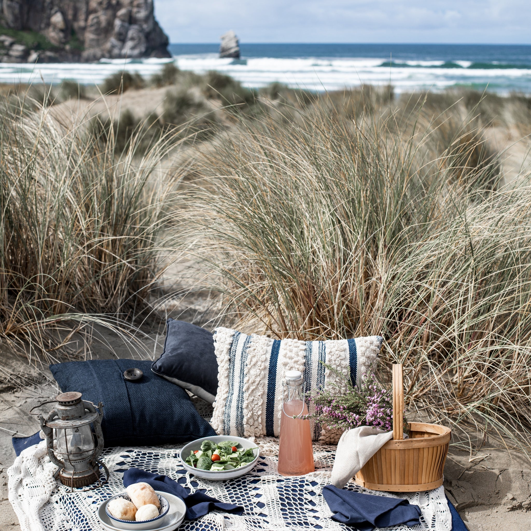 A picnic blanket and food set out in the sand dunes overlooking the sea