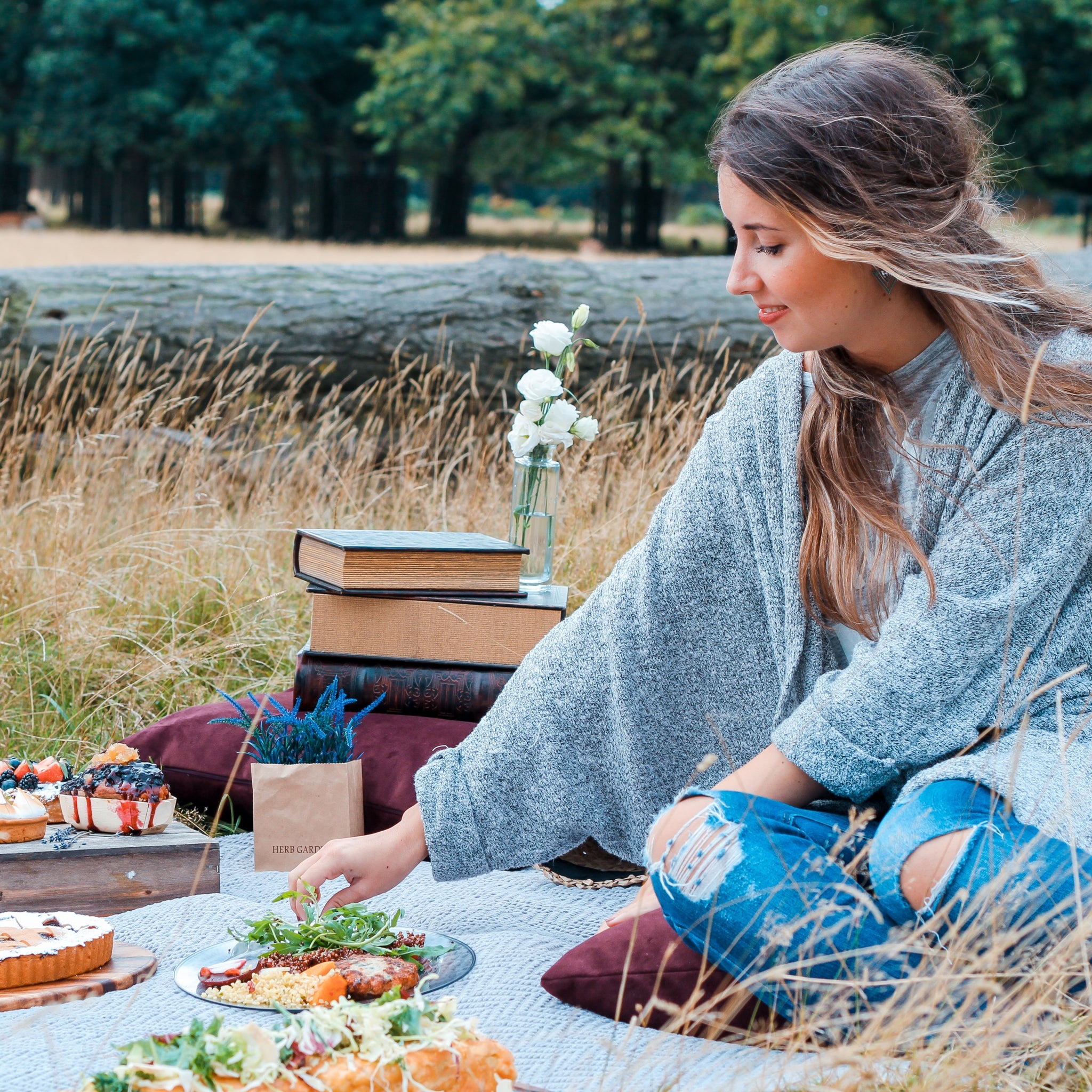 A young woman sat on a picnic blanket reaching for food