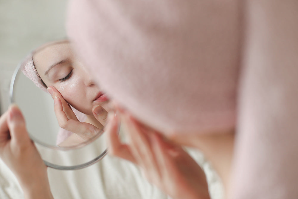 woman looking at mirror applying skin care