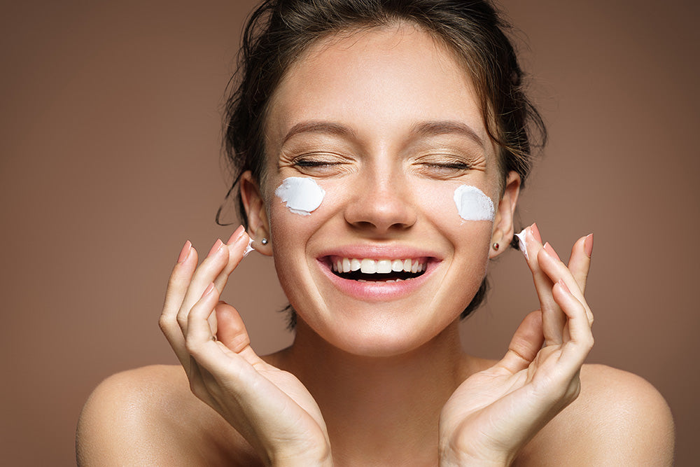 happy woman applying moisturizer on face