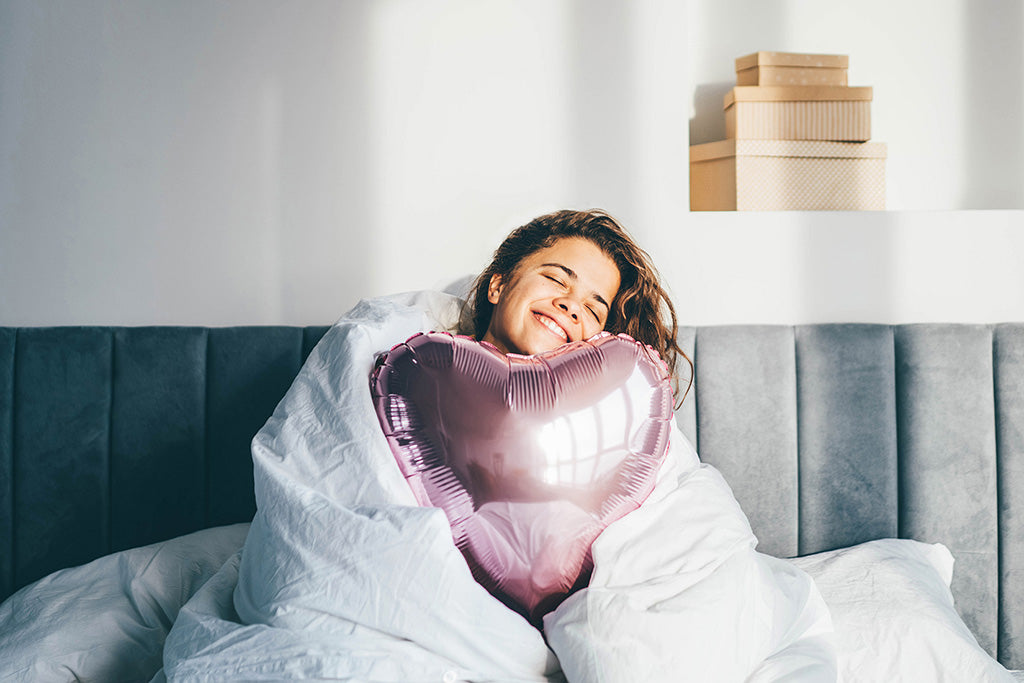 woman happy in bed hugging a heart shaped pillow