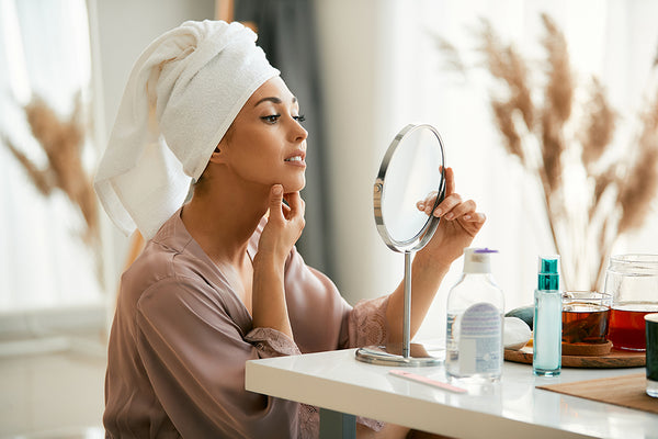 woman holding mirror applying skin care products