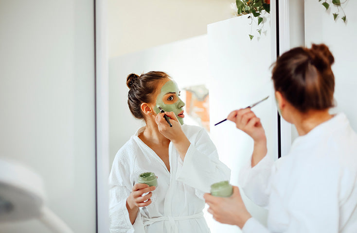 woman applying face clay mask in front of mirror