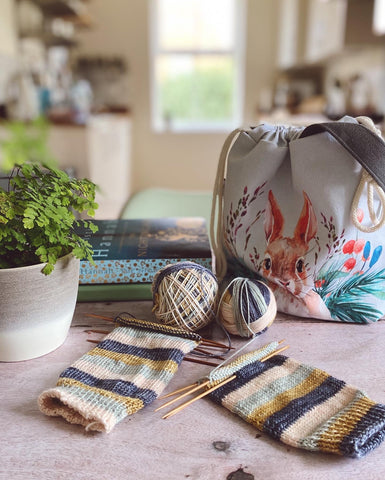 Hand knit socks mid project, sitting on a kitchen table with a knitting project bag handmade by Eldenwood Craft