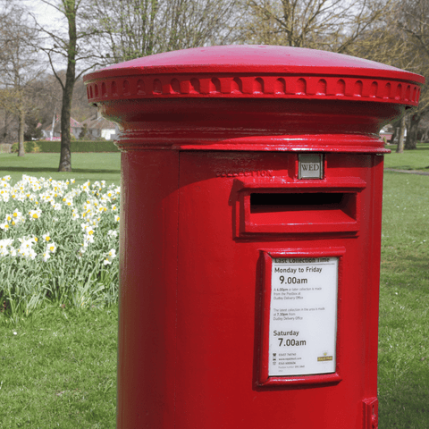 a red post box on a spring day with daffodils in the background.