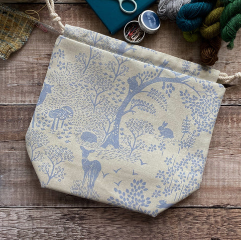 An Eldenwood Craft project bag lies on a dark table surrounded by notions and yarn. 