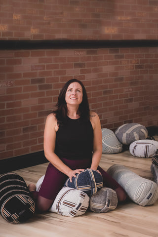 Woman sitting on 3 bolster pillows in hero yoga pose