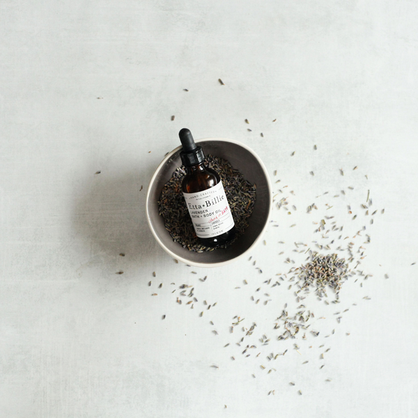 etta + billie lavender body oil in small bowl on counter with fresh lavender flowers