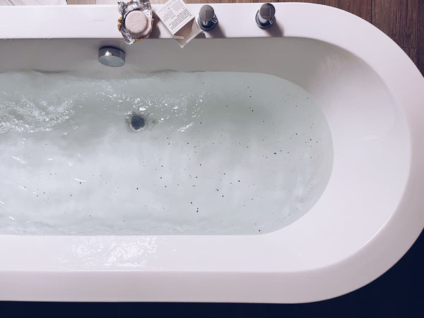 bath tub filling with water body scrub on the edge of tub