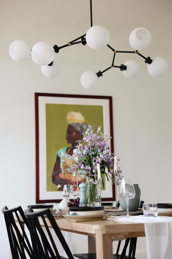 The modern black and frosted glass globed Bobbi Chandelier hangs over Jenné Claiborne's light wood dining table with a large purple flower arrangement.