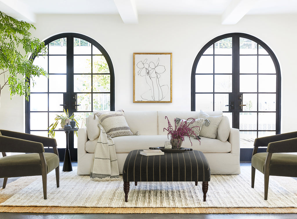 The Myla off-white slipcovered performance fabric sofa is an easy way to have a white couch with kids and pets. In front of the sofa is a black pinstriped ottoman and on either side are moss green rounded arm chairs.