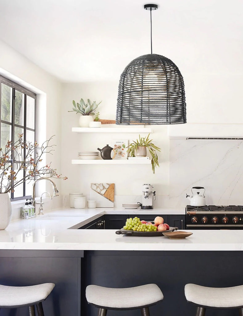 The black Beehive woven rattan pendant light hangs above a kitchen island with black cabinets and white countertops.