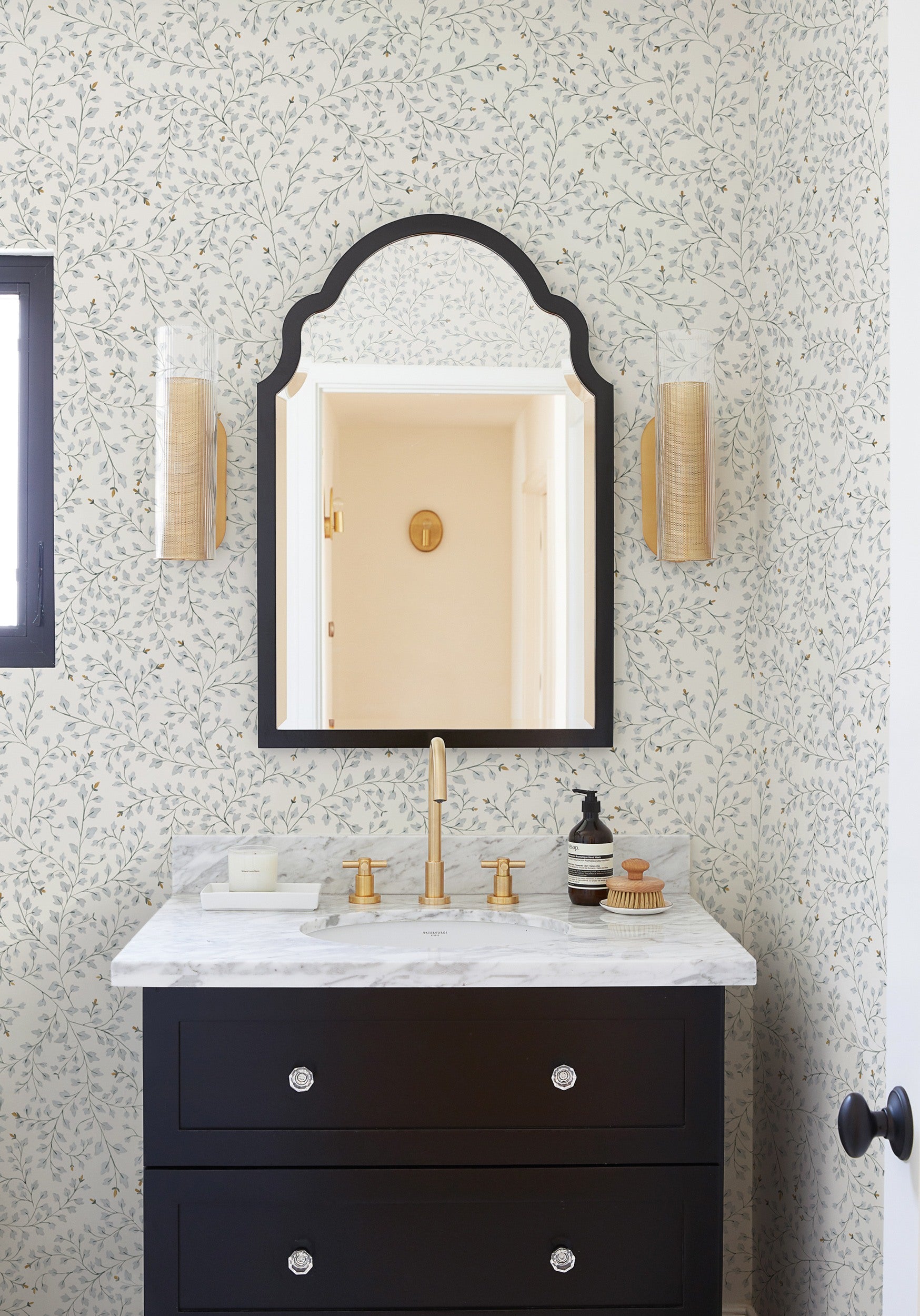 The floral Dainty Leaves wallpaper from Rylee + Cru is on display in this bathroom with a black vanity with marble top and black framed mirror.