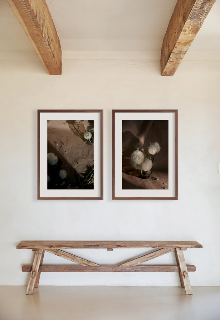 Still Life 1 and Still Life 21 photography prints by Ashley Johnson hang above a rustic wooden bench.