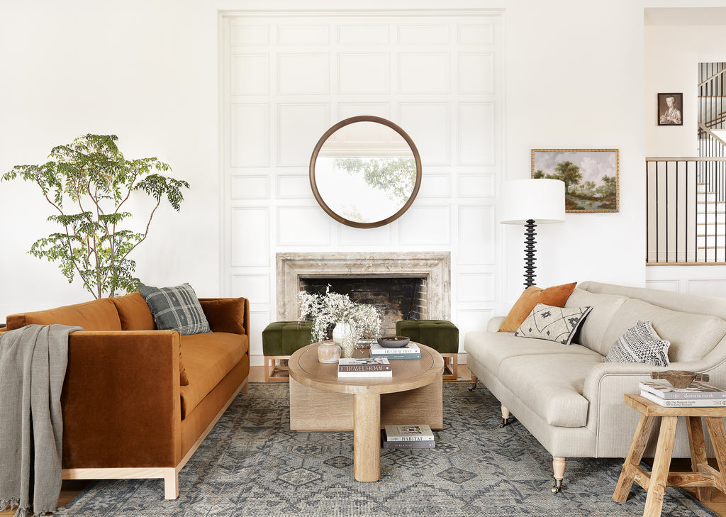 A rust velvet sofa sits across from an oatmeal linen Fabienne sofa. Both sofas have neutral black, gray and ivory throw pillows and sit on a gray geometric patterned rug.