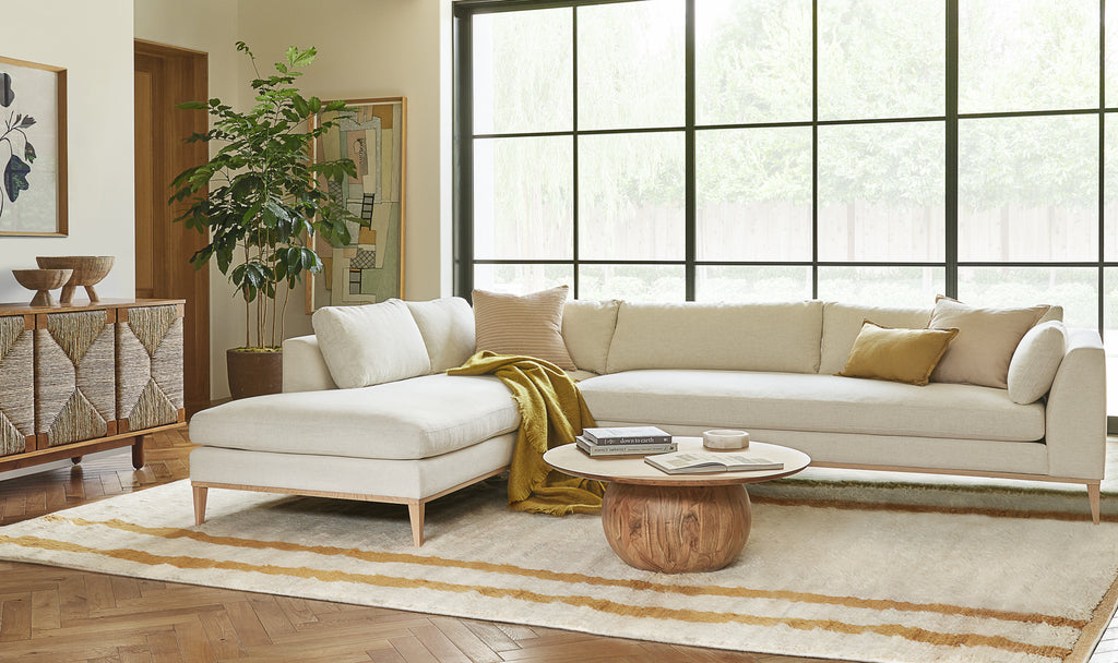 The Ojai black and cream square throw pillow and two Arlo throw pillows - one lumbar pillow in mustard and a square pillow in light pink - sit atop a modern ivory sofa with chaise in a warm modern living room look.