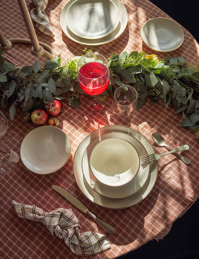 The Heather Home Katherine Red Plaid Tablecloth anchors this holiday table with a white place setting, wine glass and apples.