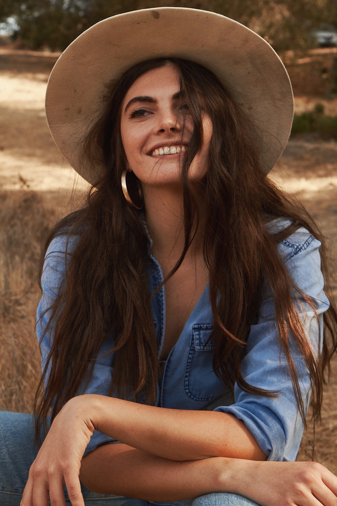 Savannah Di Marco, founder of Sorella Collective, wears a wide brimmed hat and a denim button-up shirt.