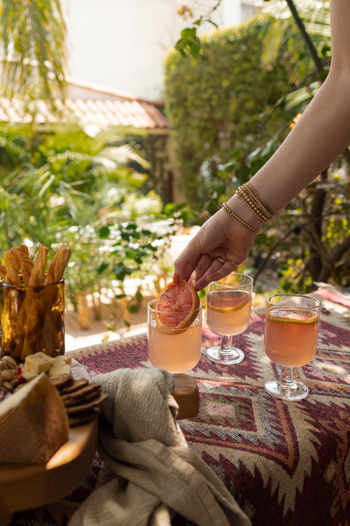 Interior designer Lexie Layne Sokolow places a slice of blood orange into a glass of blood orange margarita with two other glasses next to it.