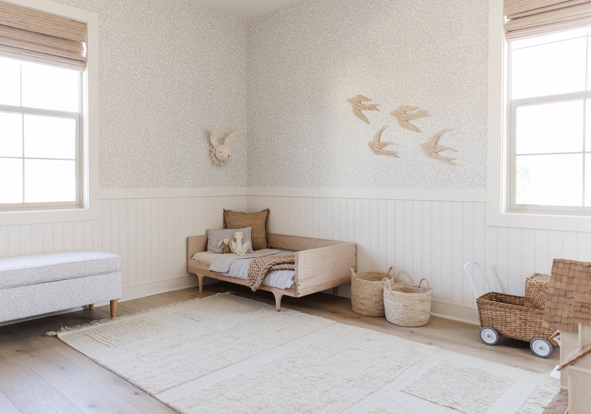 Dainty Leaves wallpaper from Rylee + Cru is the backdrop for a toddler room with a small, light wood bed with light blue bedding, rattan toy baskets, and rattan bird wall sculptures.