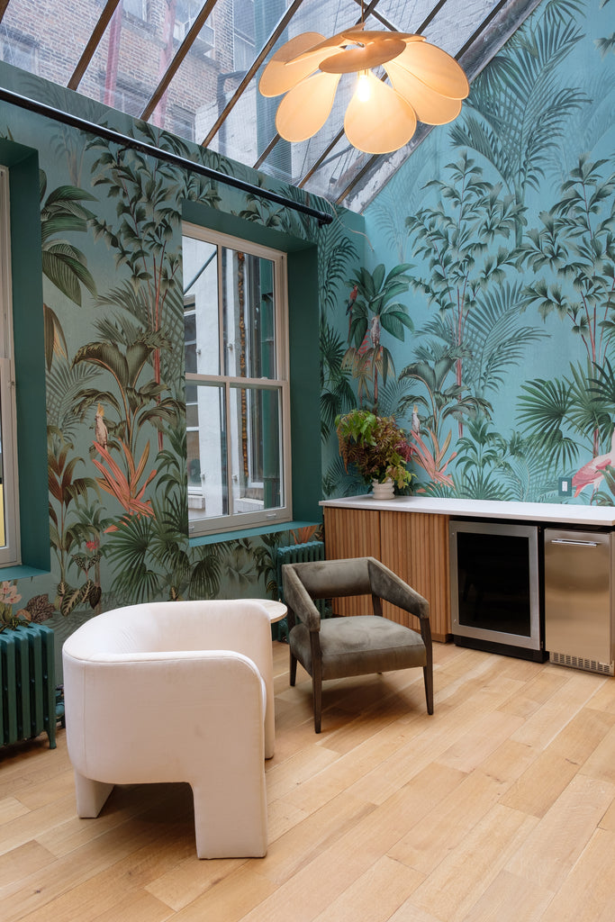 A curved white barrel chair sits next to a dark green velvet Lyssa accent arm chair next to a counter. Blue tropical wallpaper covers the walls.